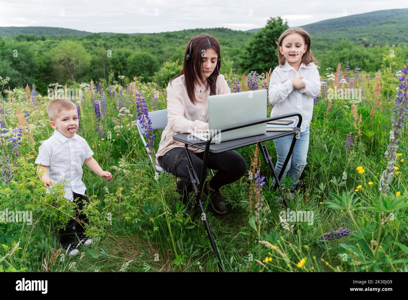Playful children by mother working on laptop in meadow Stock Photo