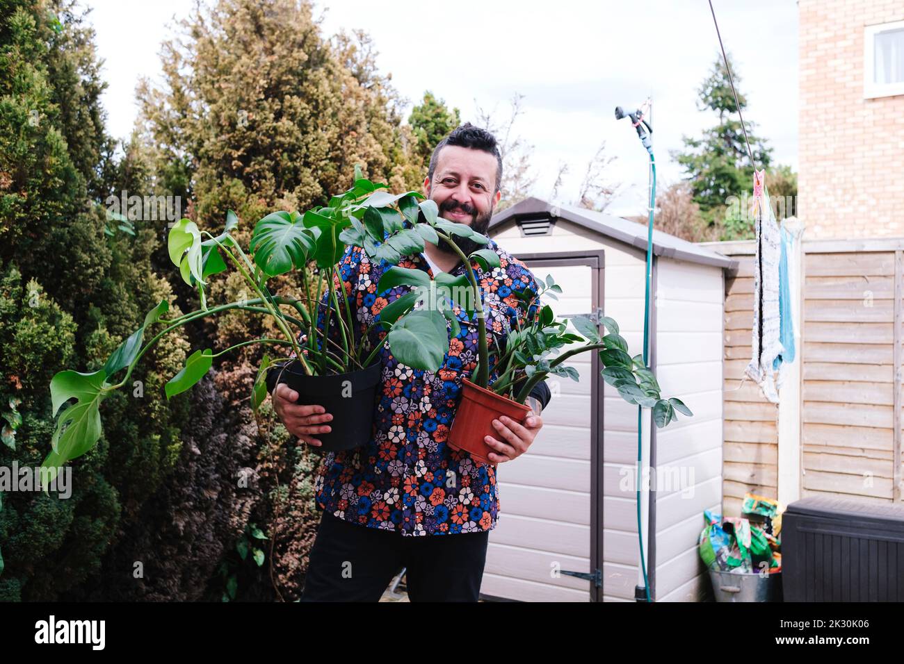 Smiling man with potted plants standing in back yard Stock Photo