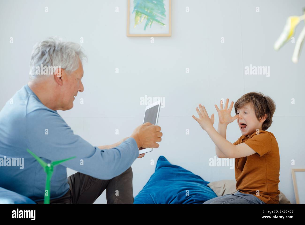 Senior man photographing playful grandson through tablet PC at home Stock Photo