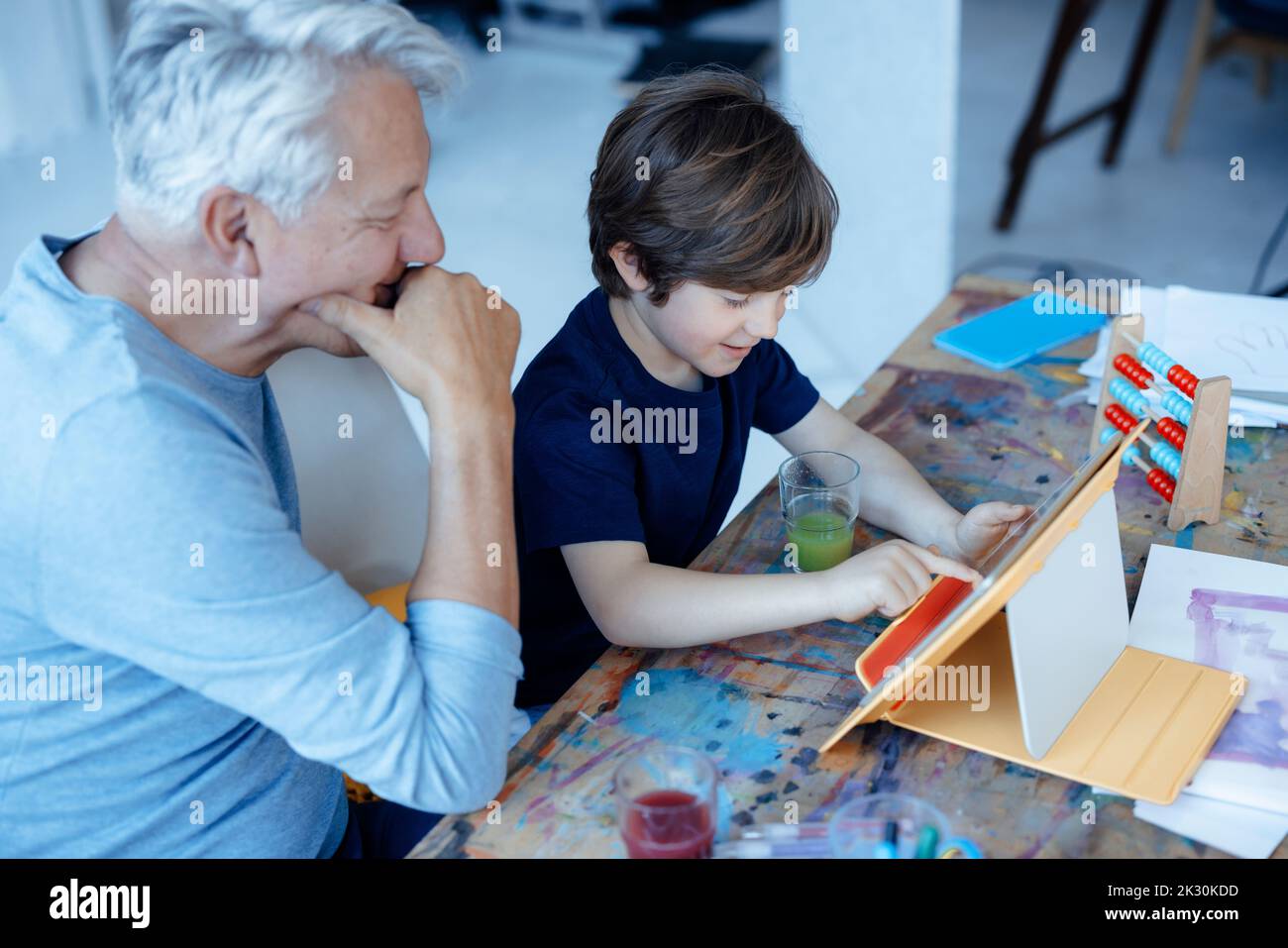 Smiling boy using tablet PC by grandfather at home Stock Photo