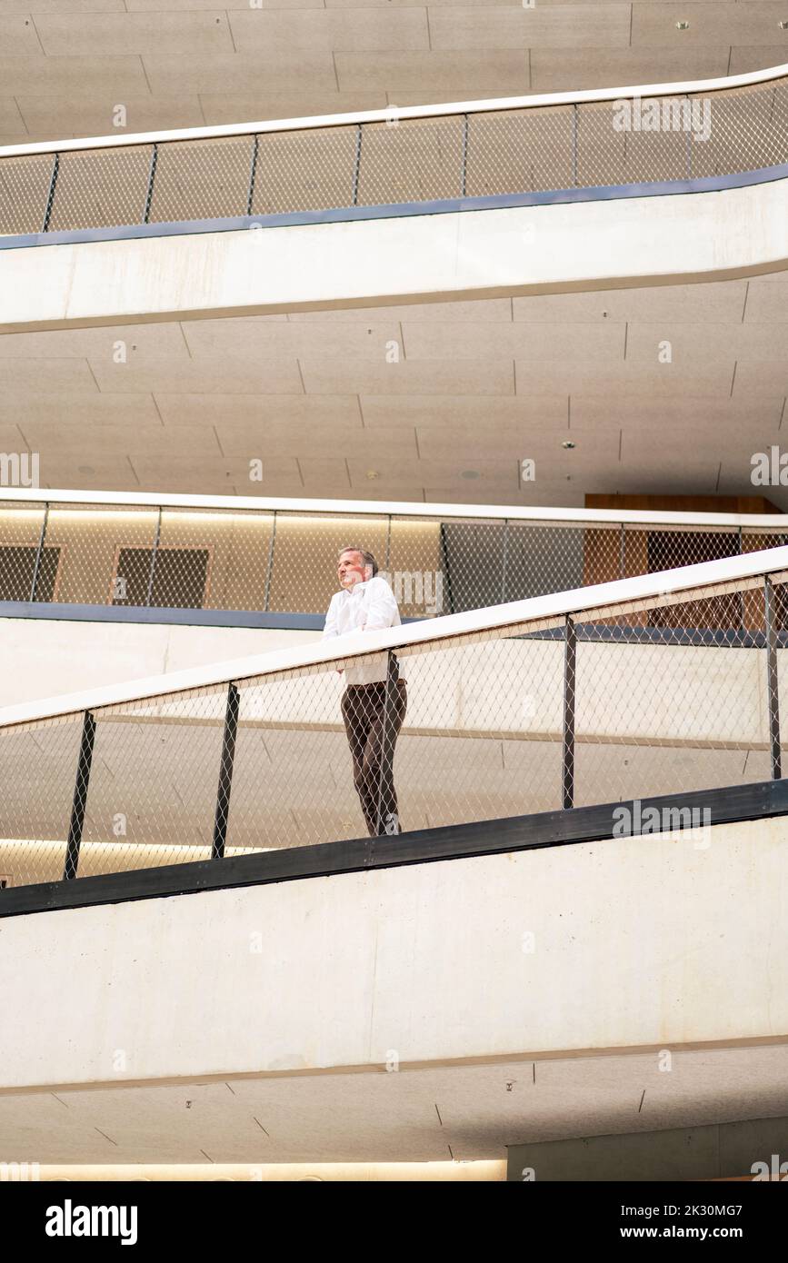Businessman leaning on railing in corridor of office Stock Photo - Alamy