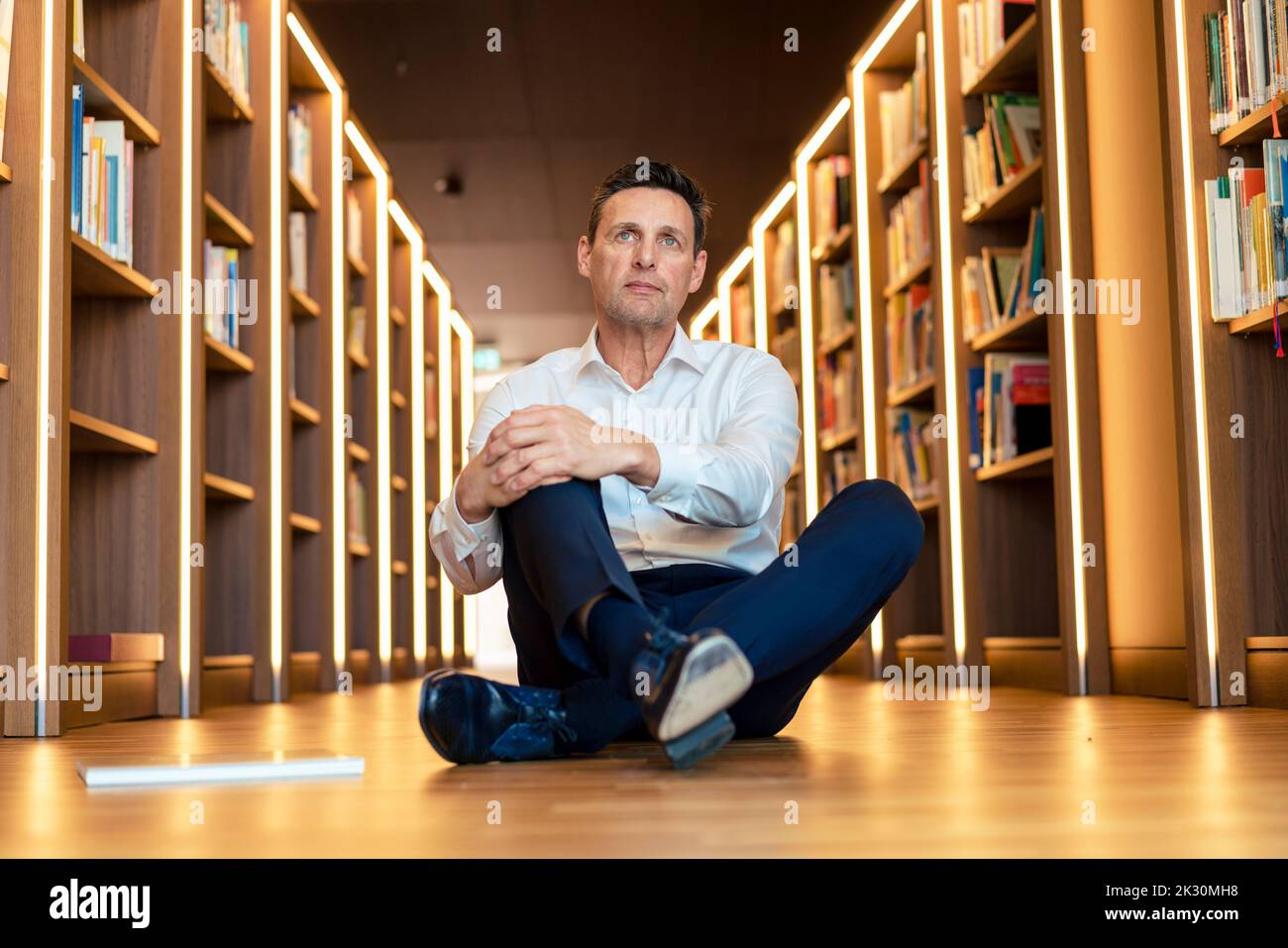 Contemplative man sitting on floor in illuminated library Stock Photo