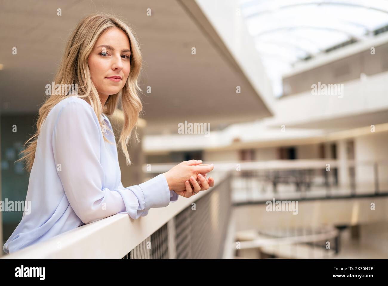 Confident businesswoman leaning on railing in corridor Stock Photo - Alamy