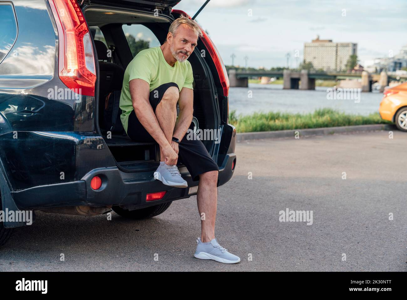 Mature man tying shoelace sitting in car trunk Stock Photo