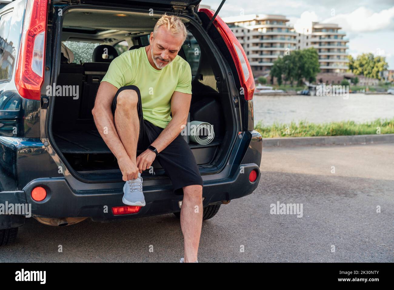 Man tying shoelace sitting in trunk of car Stock Photo