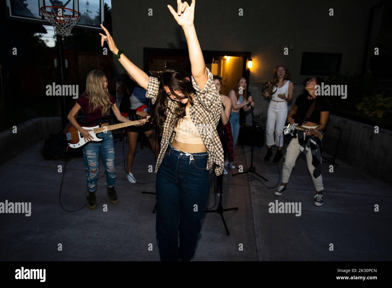 Carefree teenage girl dancing with friends playing music in driveway