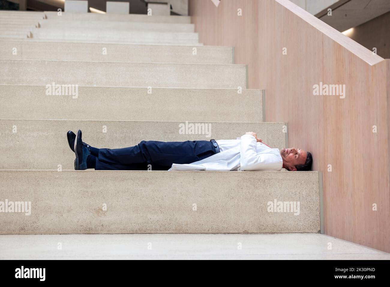 Overworked mature doctor lying on step in hospital Stock Photo