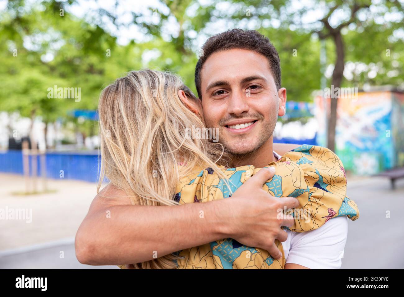 Smiling man hugging girlfriend at park Stock Photo
