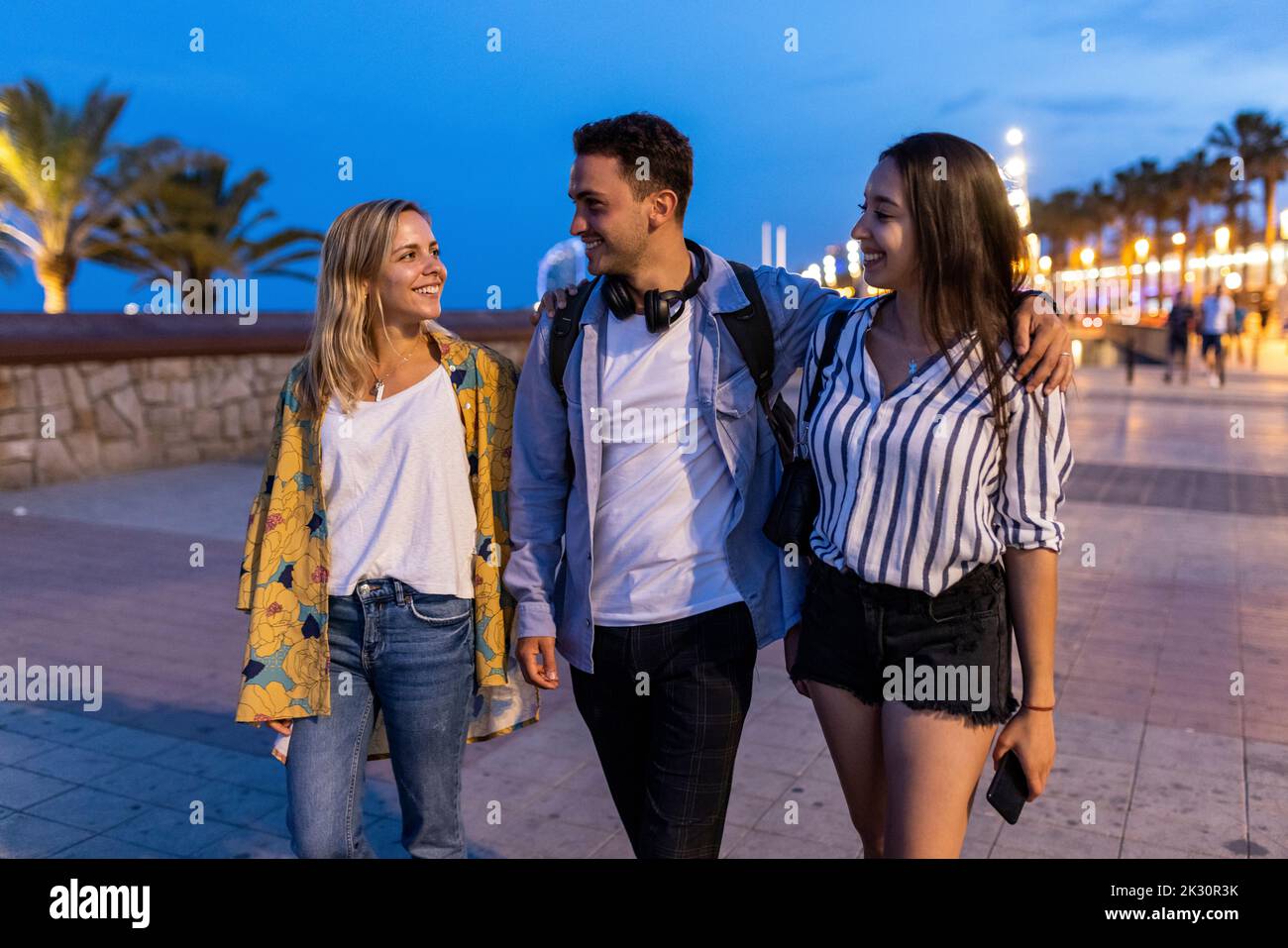 Smiling young man with women walking at promenade Stock Photo - Alamy