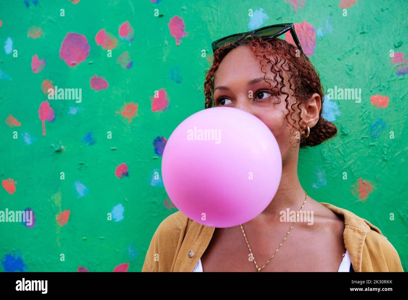 Young woman blowing bubble gum in front of wall Stock Photo - Alamy