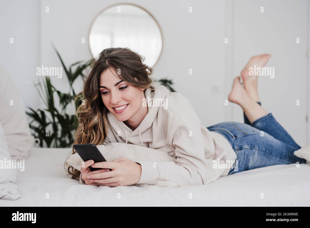 Smiling woman lying on bed texting through smart phone Stock Photo