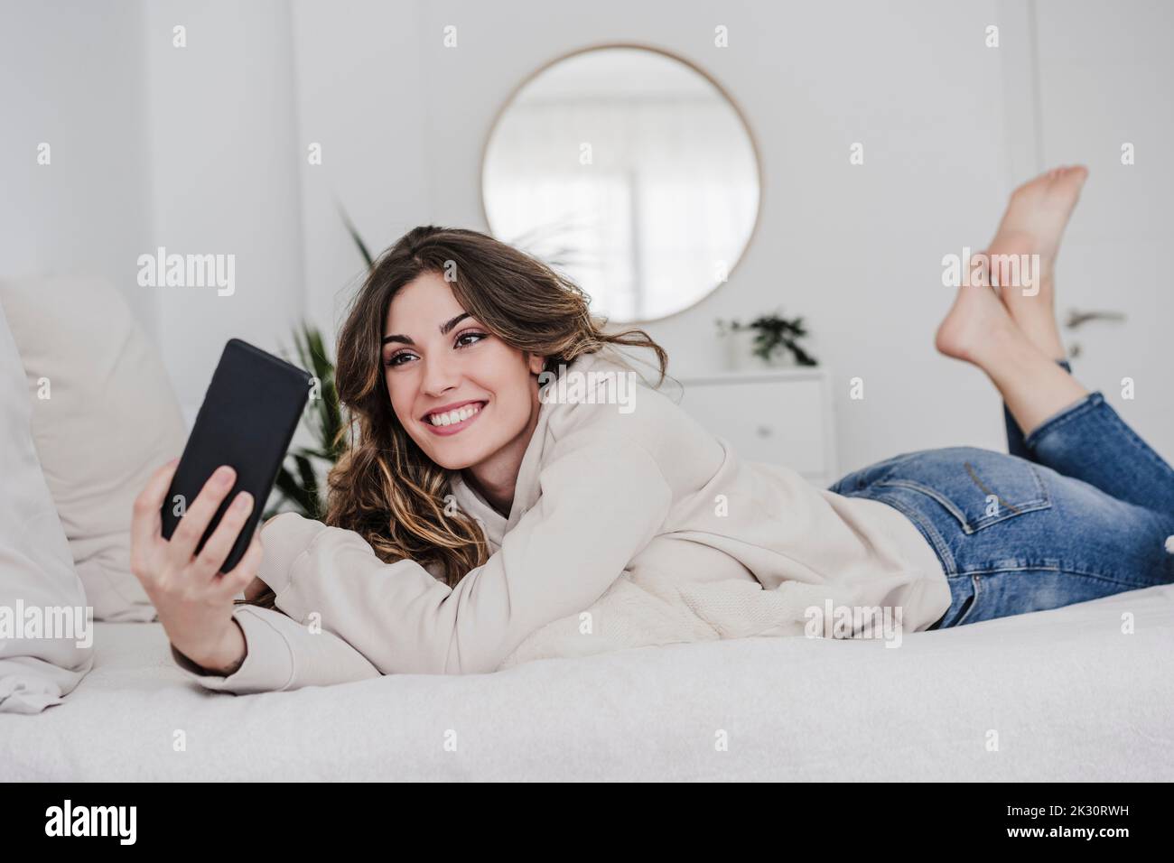 Happy young woman taking selfie through smart phone lying on bed at home Stock Photo