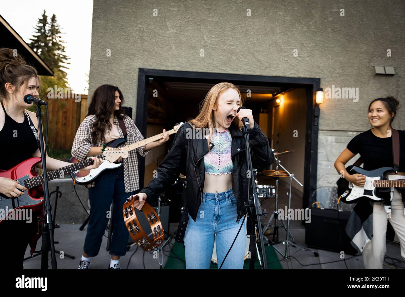 Teenage girl friends singing and playing electric guitars in driveway