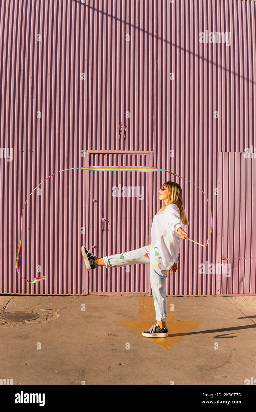 Woman balancing on one leg doing rhythmic gymnastics in front of corrugated wall Stock Photo