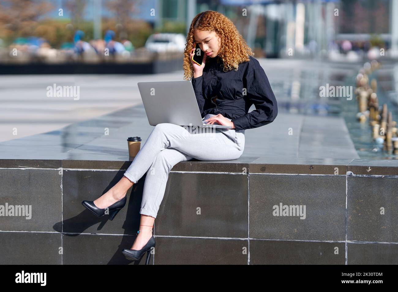 Young freelancer using laptop and talking on smart phone Stock Photo