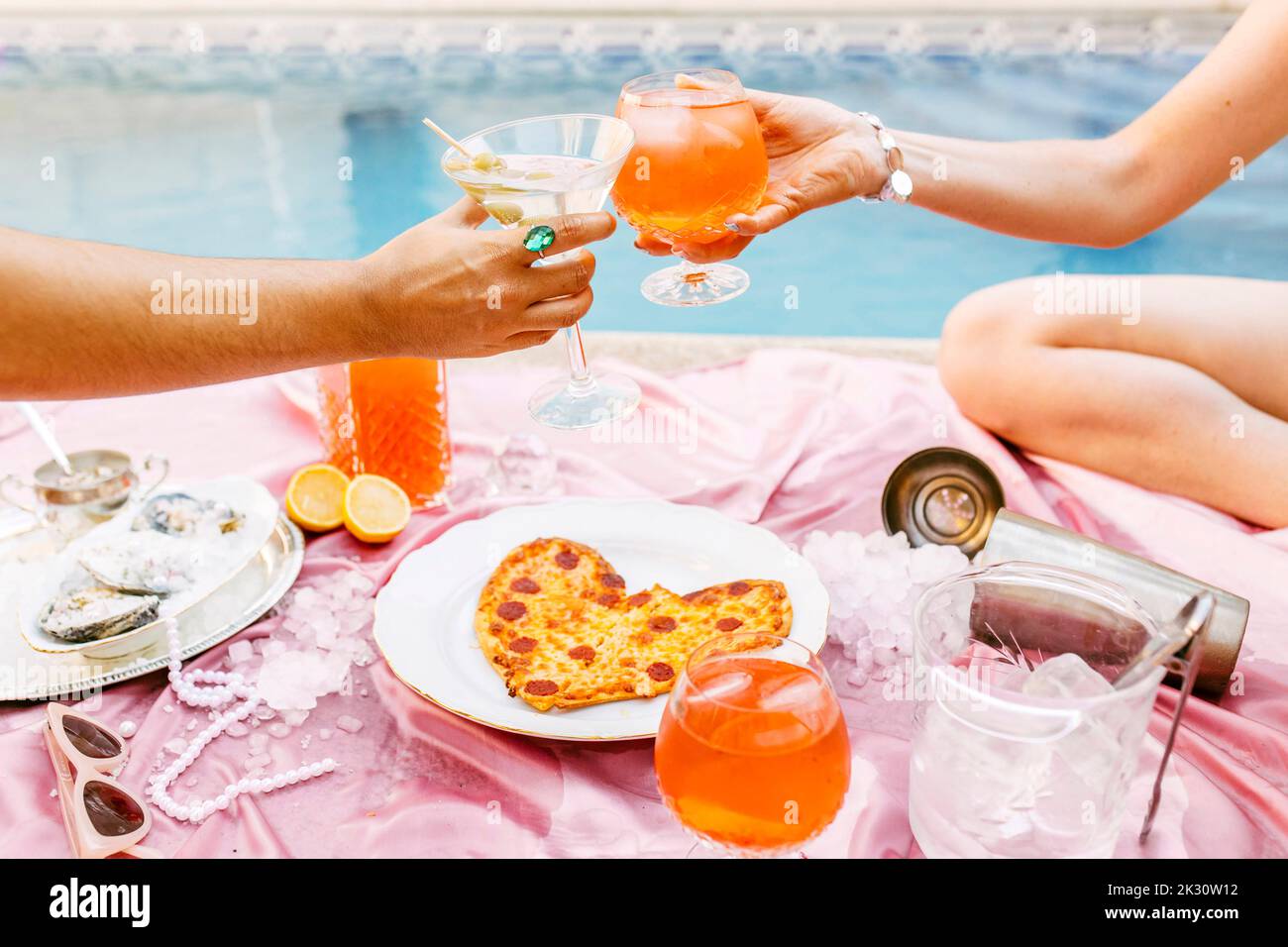 Friends toasting cocktails over heart shaped pizza at poolside Stock