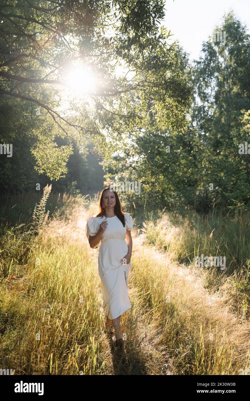 Woman wearing white dress standing in forest on sunny day Stock Photo ...