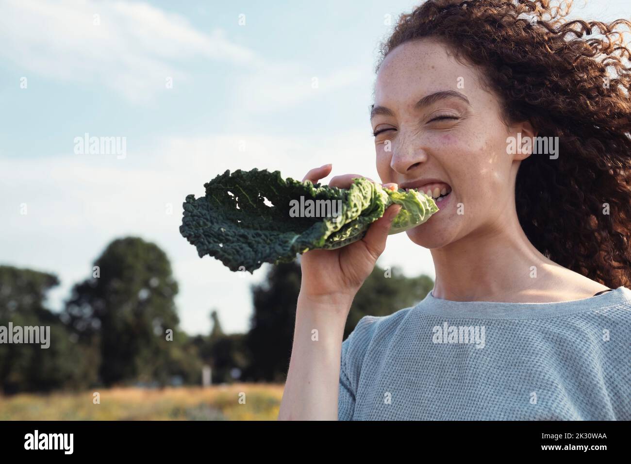 Woman with curly hair biting kale leaf Stock Photo