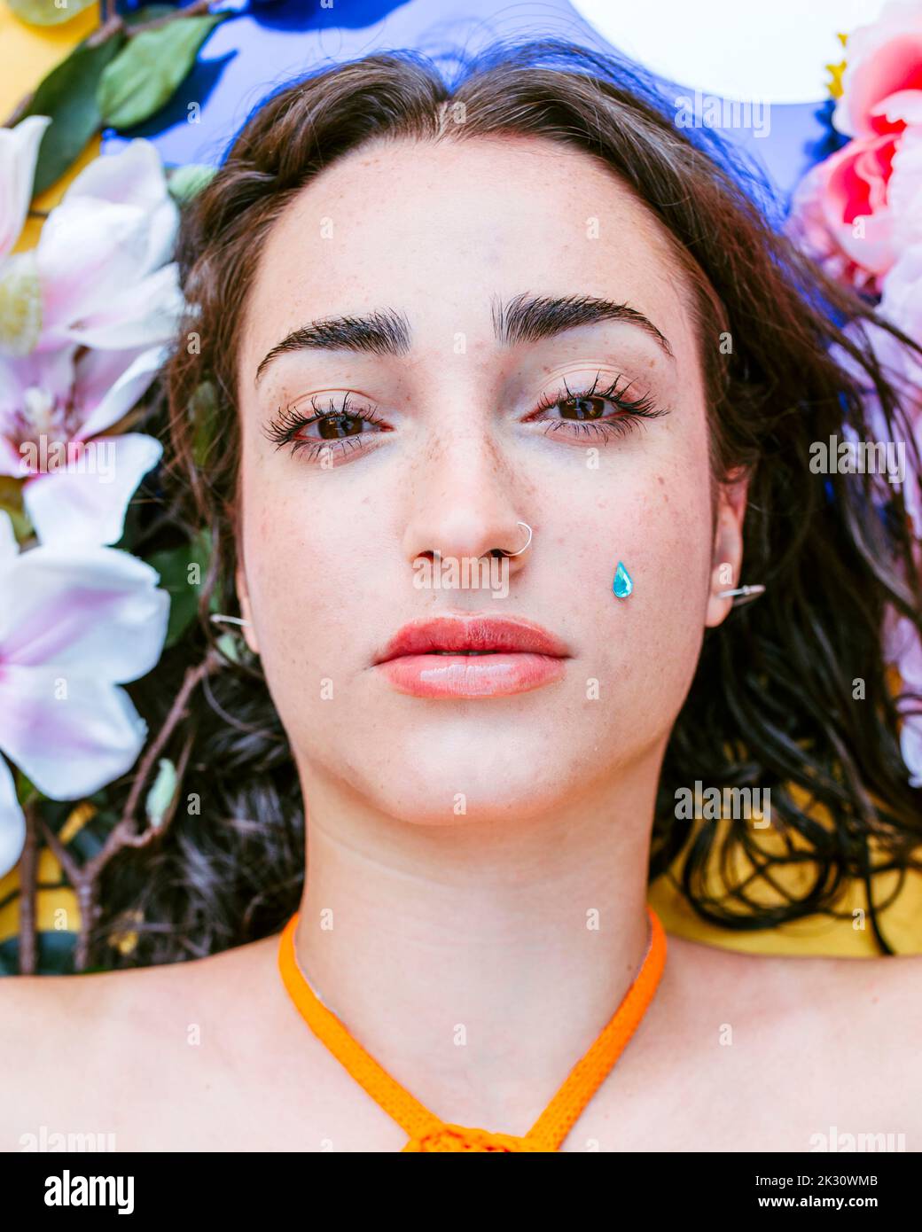 Sad young woman lying on flowers with teardrop sticker Stock Photo