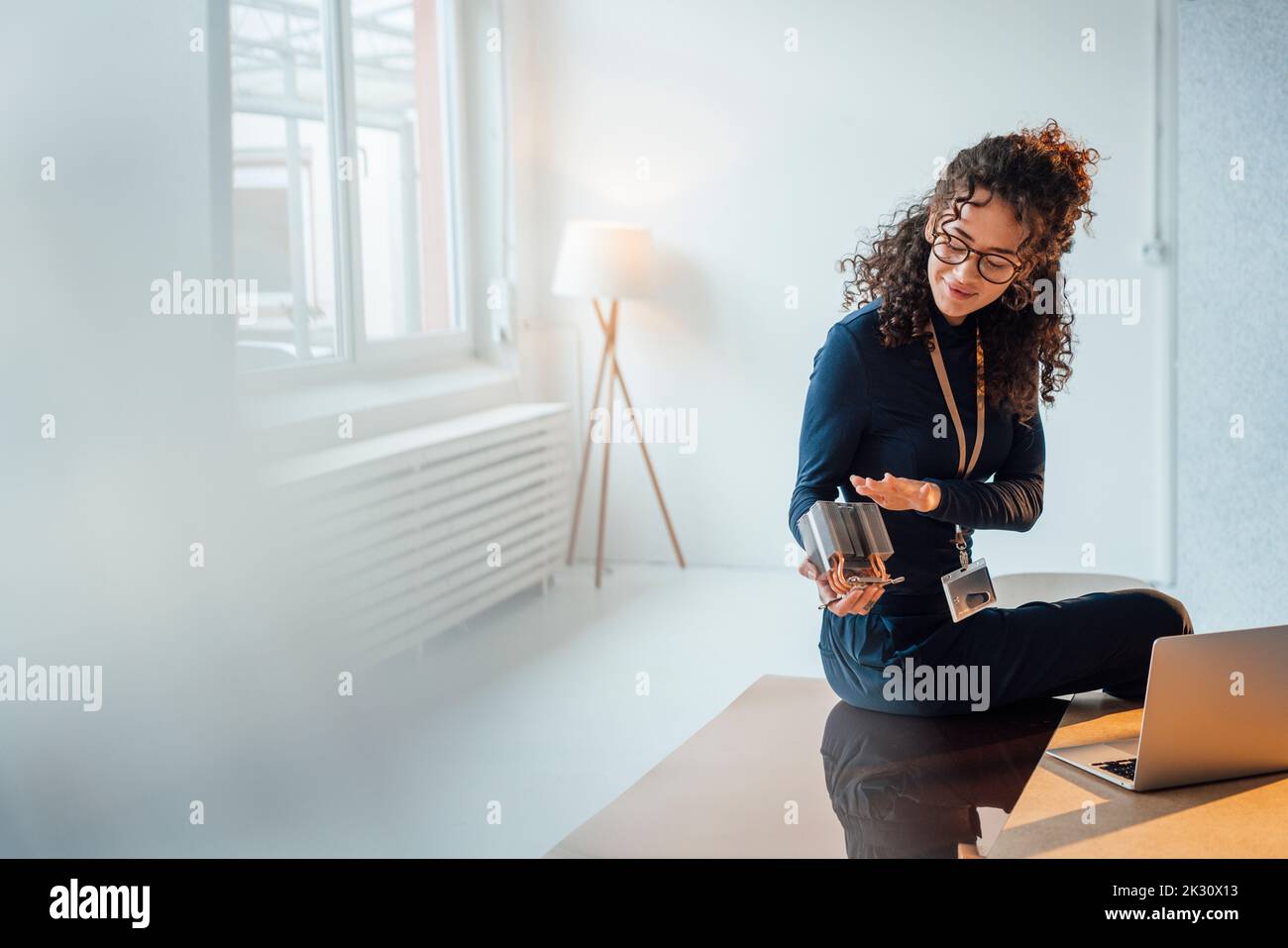 Smiling young engineer analyzing semiconductor sitting on desk in office Stock Photo