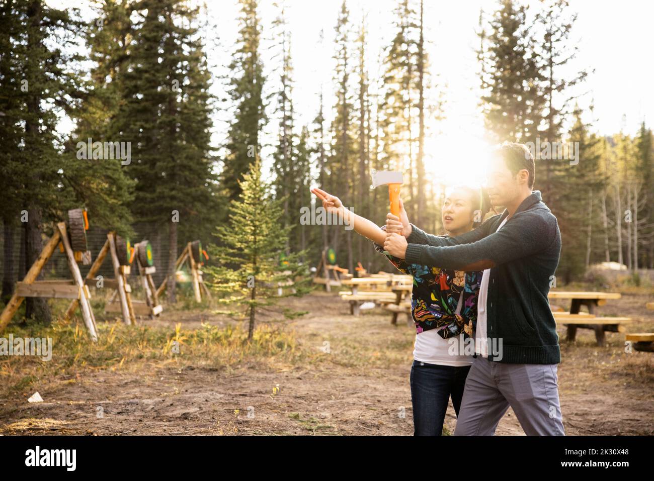Woman showing man how to throw axe at target in forest Stock Photo