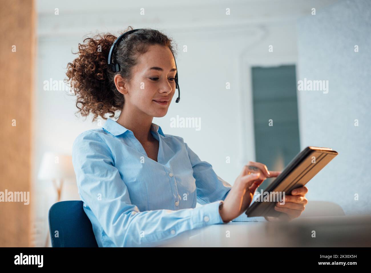 Smiling customer service representative using tablet PC sitting at desk in office Stock Photo