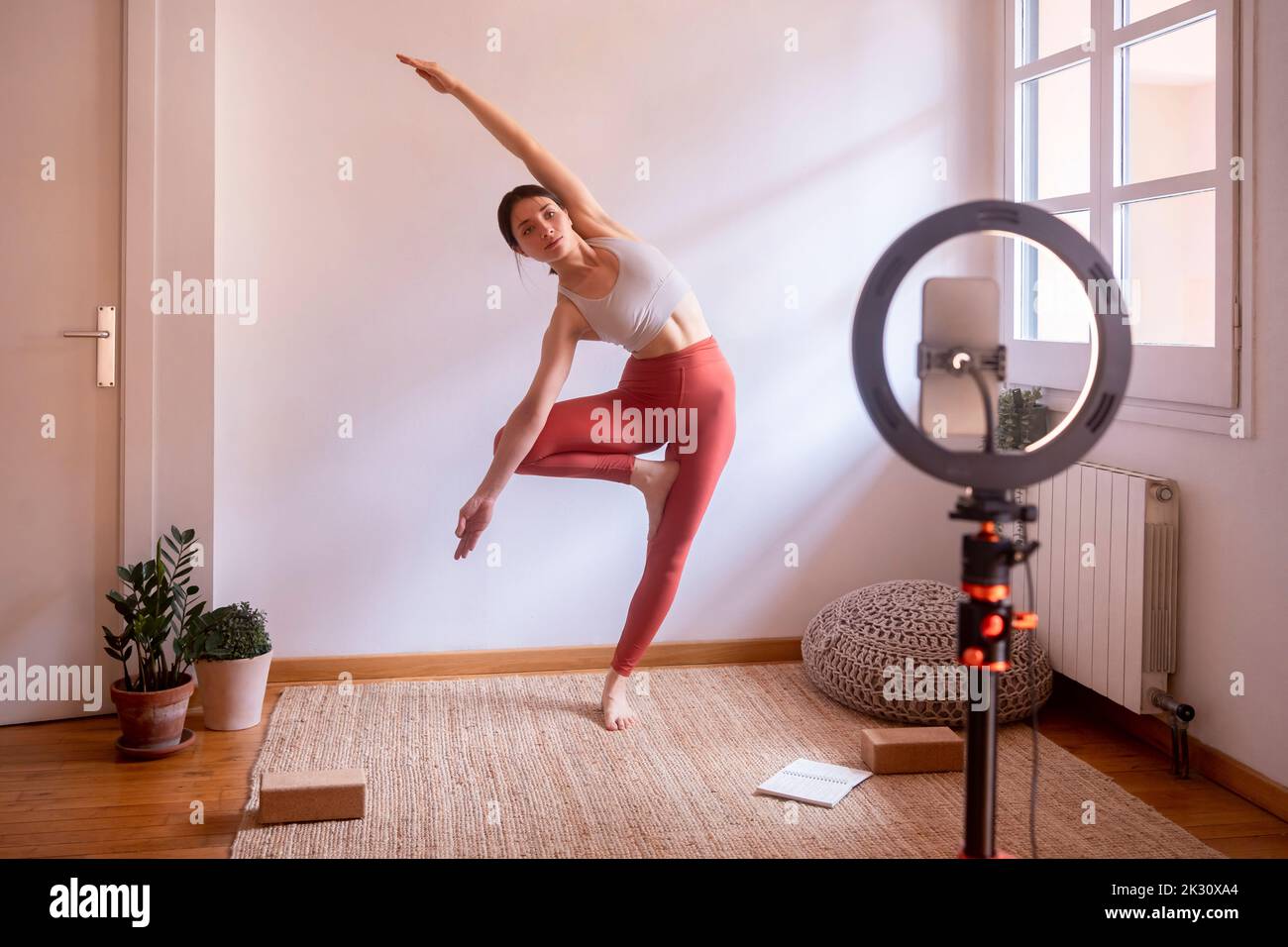 Influencer in tree position standing on one leg taking online yoga class at home Stock Photo