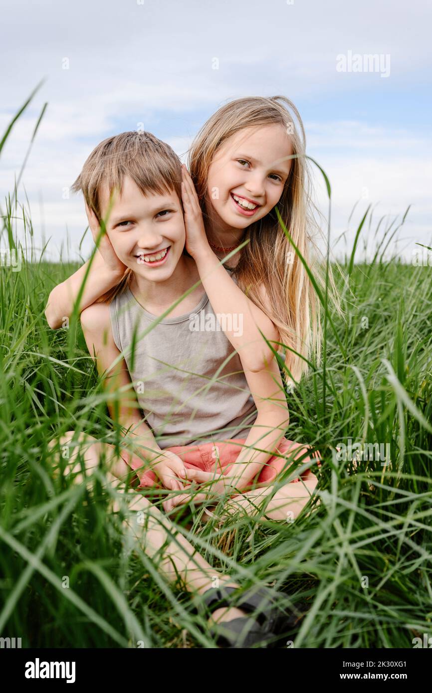 Girl covering ears of brother amidst green grass Stock Photo Alamy