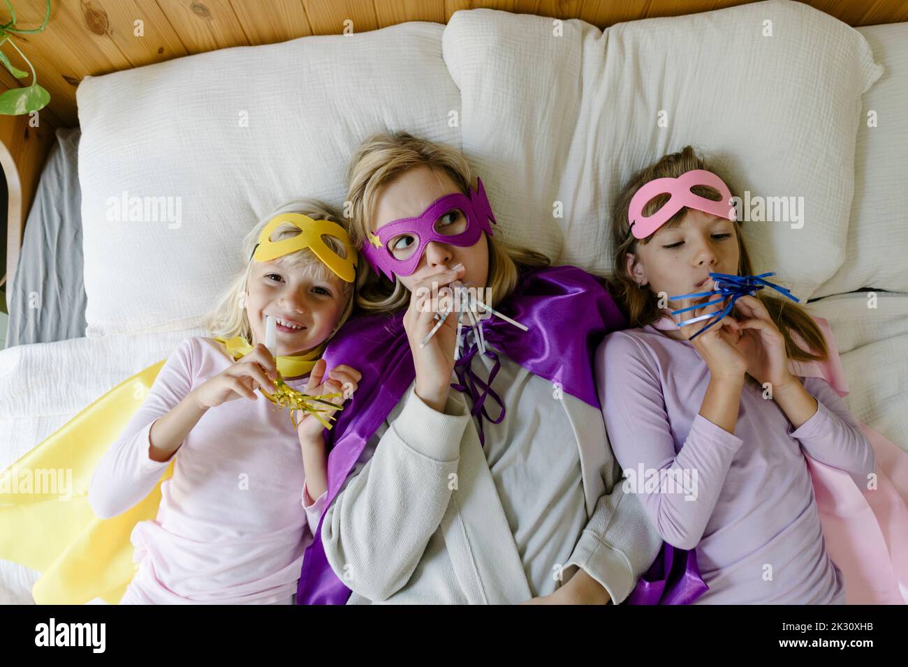 Mother and daughters with party horn blower lying on bed at home Stock ...