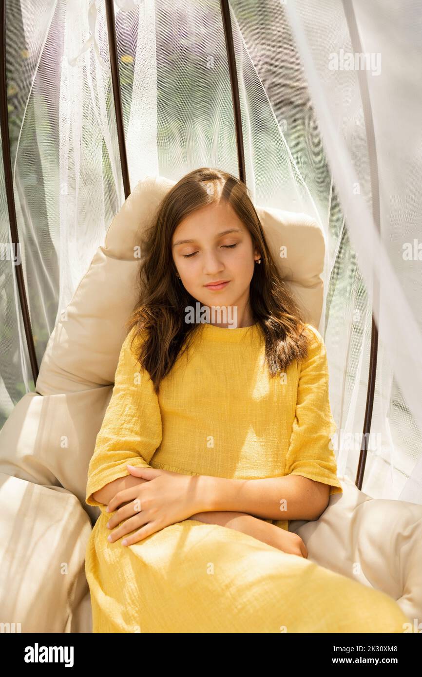 Girl with eyes closed sitting in hanging chair Stock Photo - Alamy