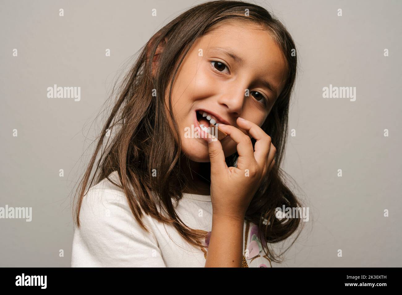 Cute girl eating chocolate against gray background Stock Photo