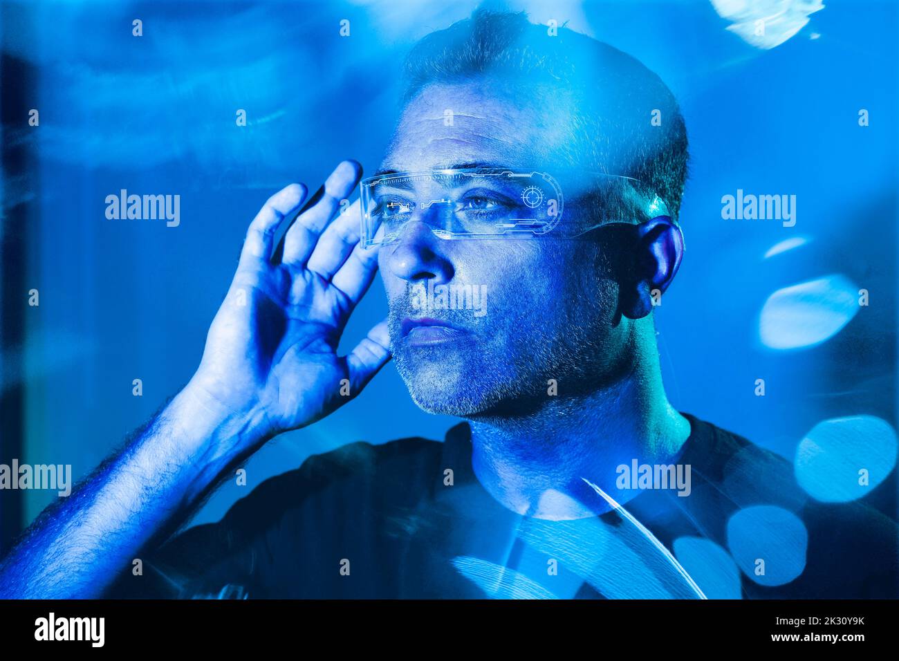 Man adjusting futuristic glasses illuminated with blue light Stock Photo