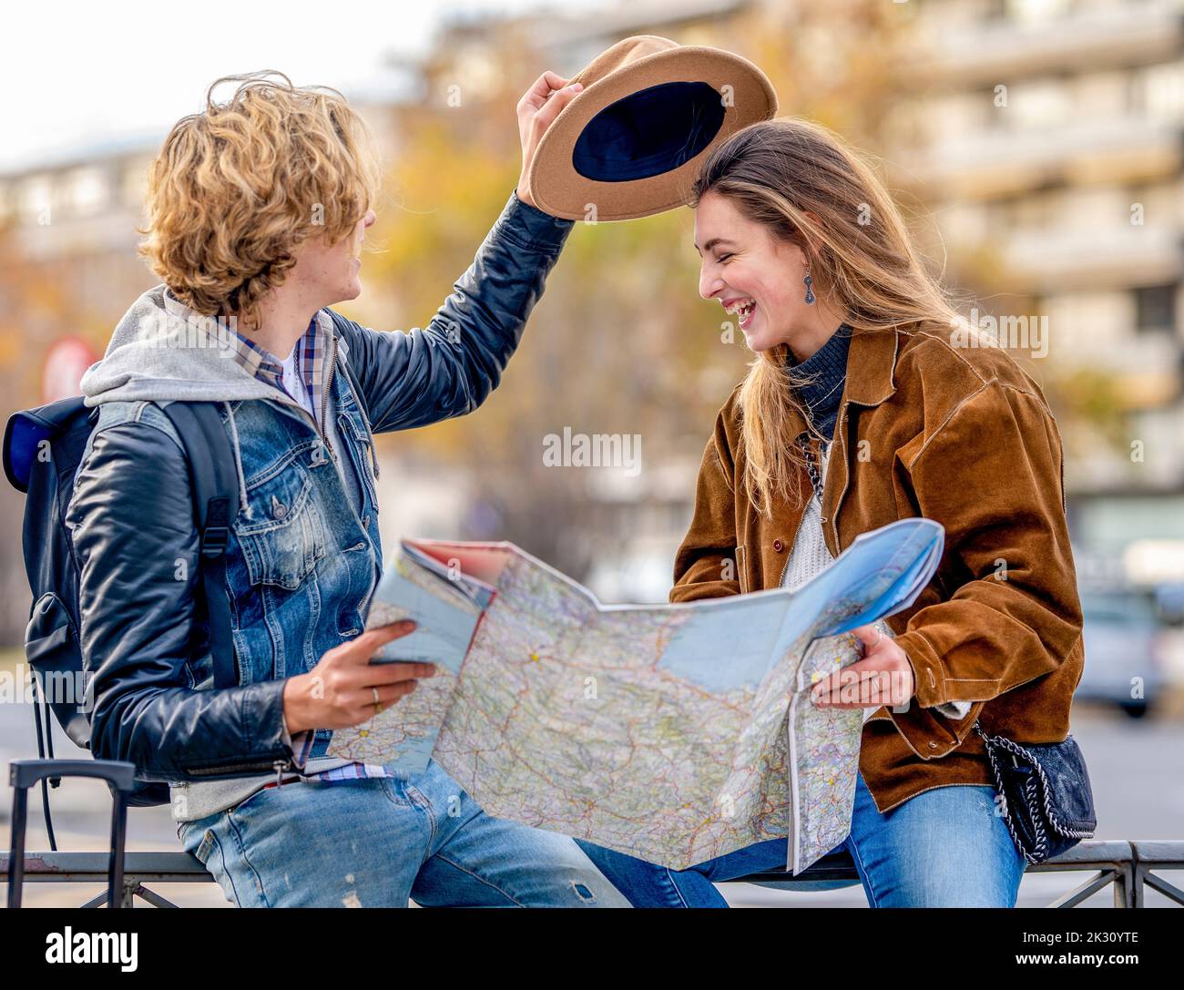 Young man holding hat and map sitting on railing with woman Stock Photo