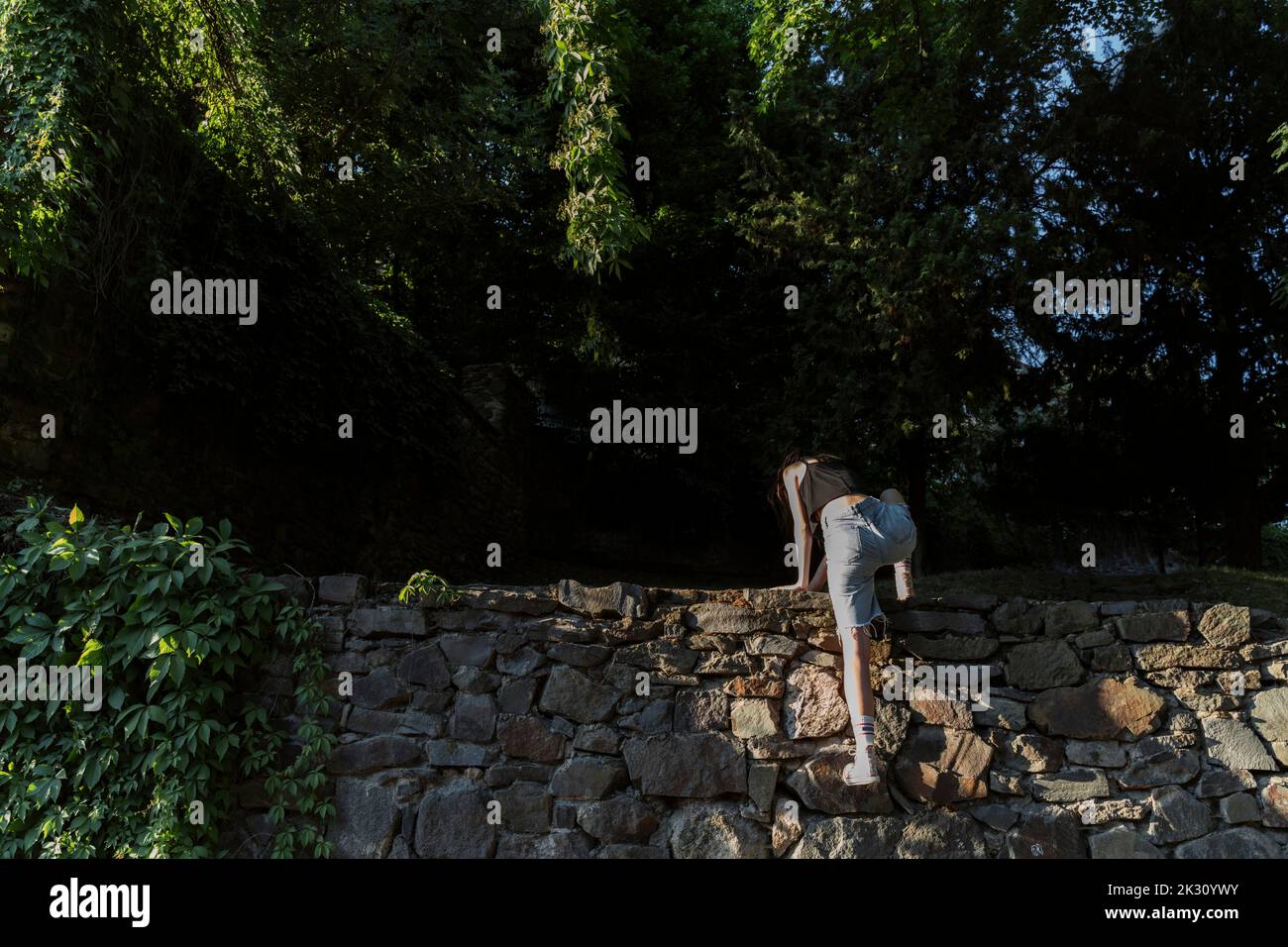 Non-binary person climbing on stone wall Stock Photo