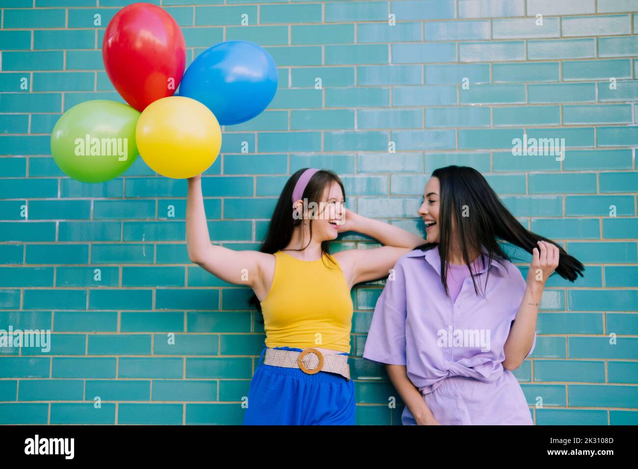 Woman holding multi colored balloons standing by friend with in front of wall Stock Photo