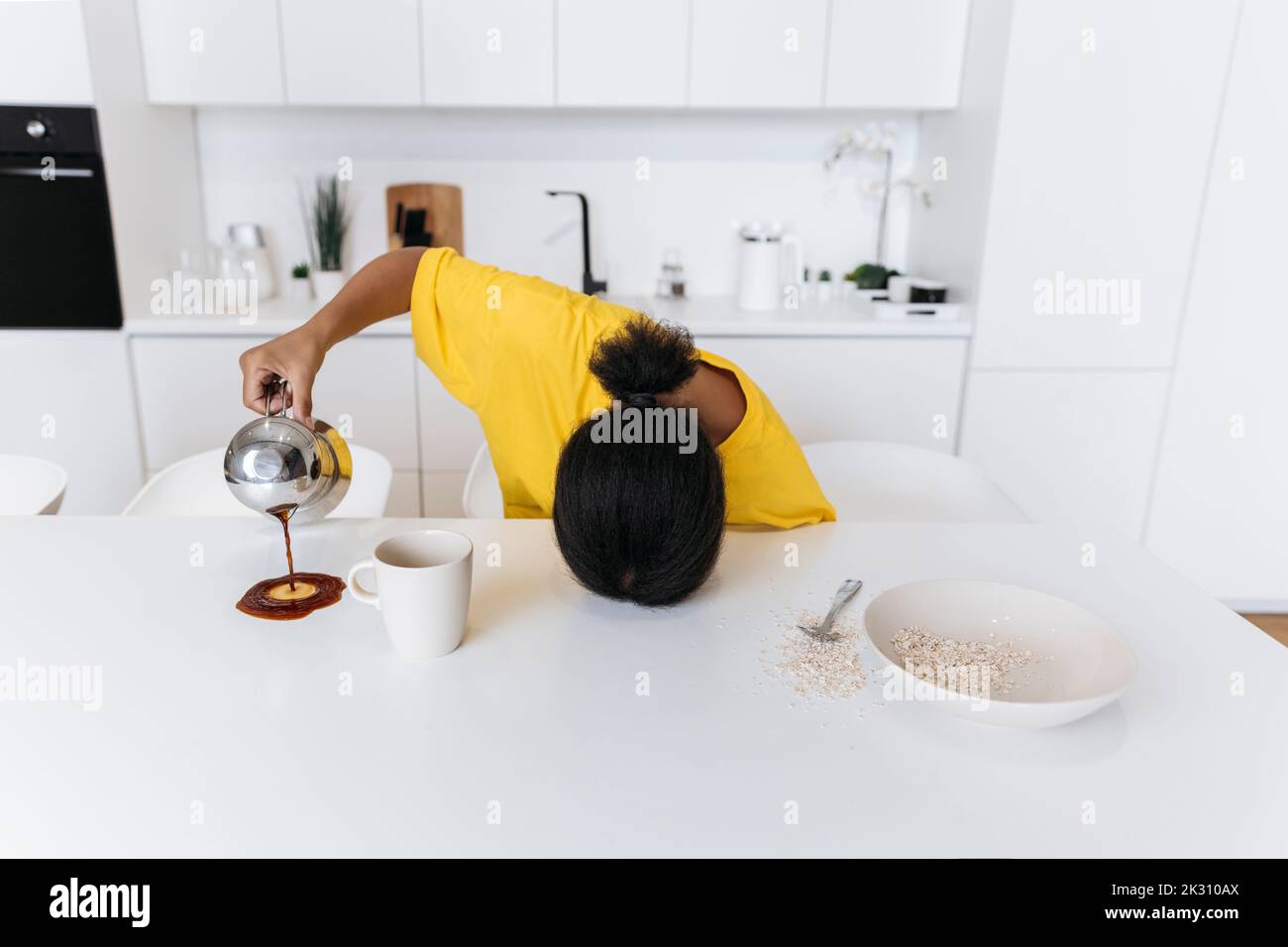 Exkausted woman spilling coffee on kitchen table Stock Photo