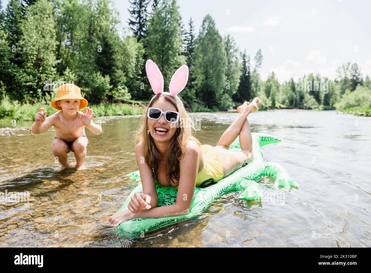 Happy woman relaxing on inflatable crocodile by son playing in water Stock Photo