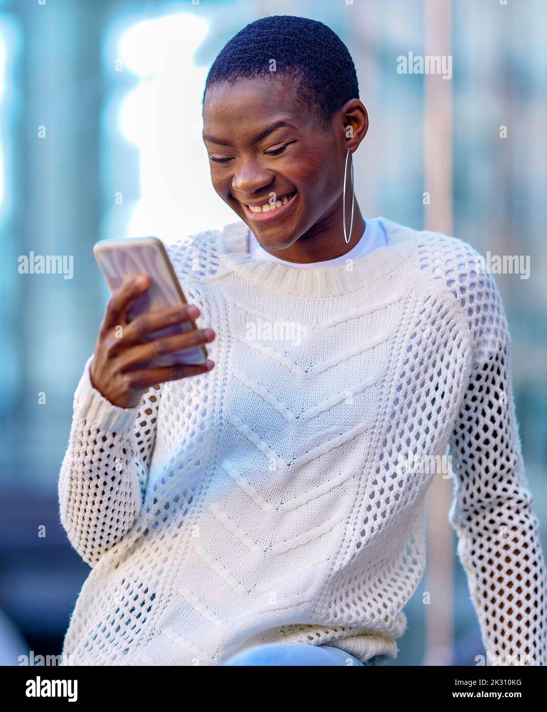 Woman wearing hoop earring looking at smart phone and smiling Stock Photo