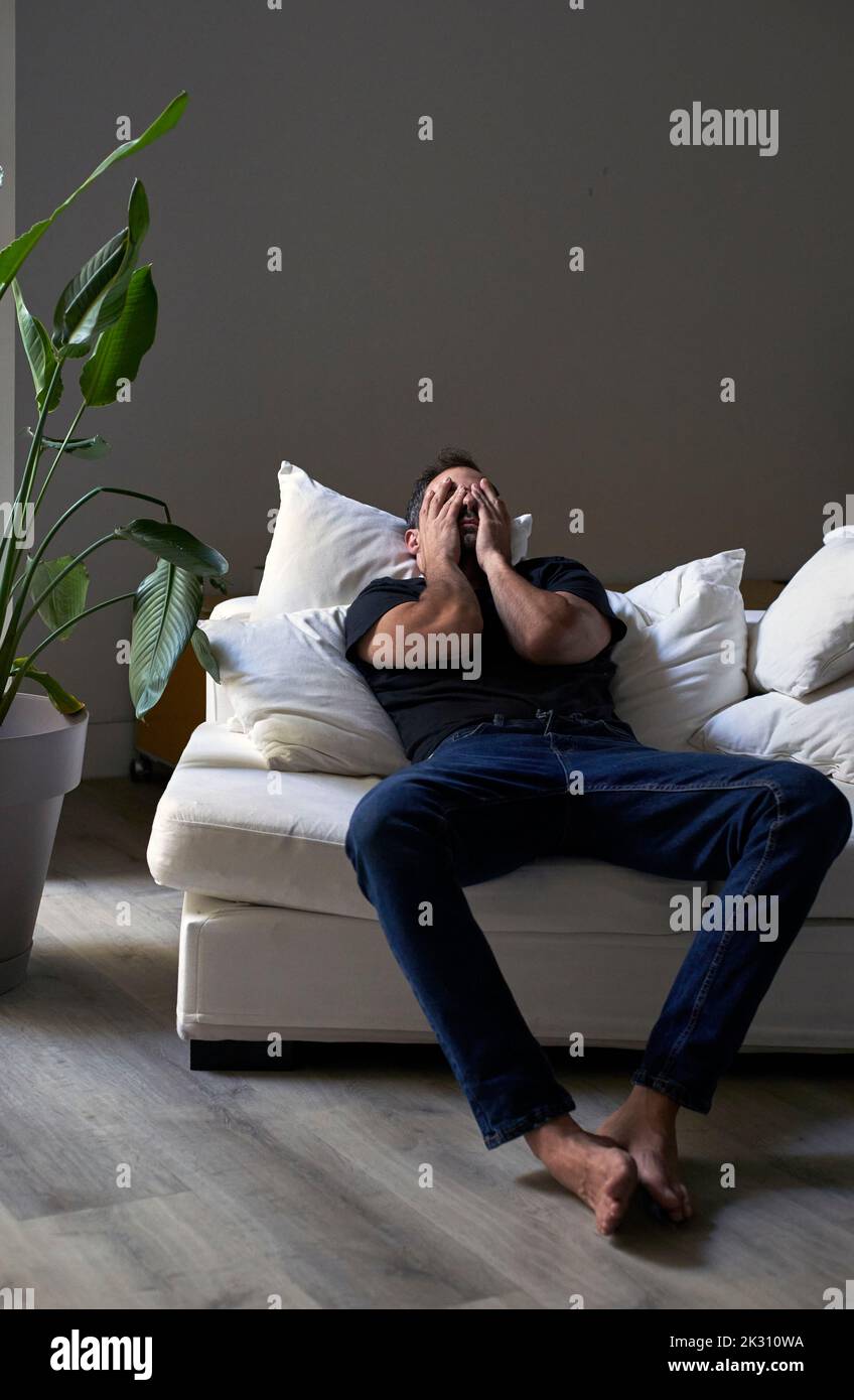 Depressed man covering face with hands lying on sofa Stock Photo