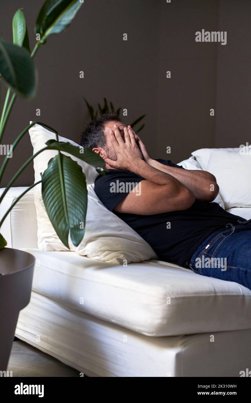 Sad man covering face with hands by lying on sofa Stock Photo