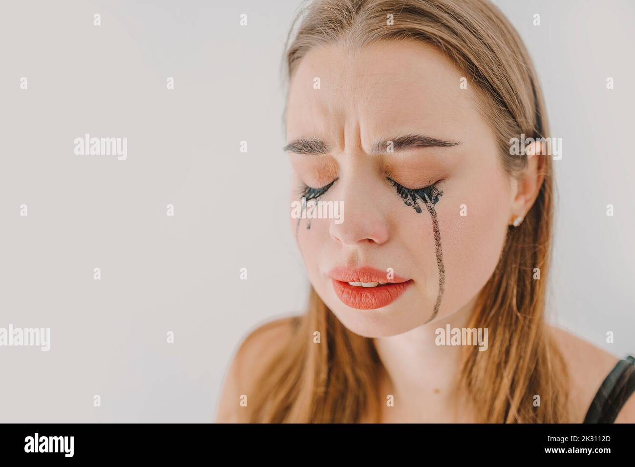 Sad young woman with smudged mascara crying in front of wall Stock Photo
