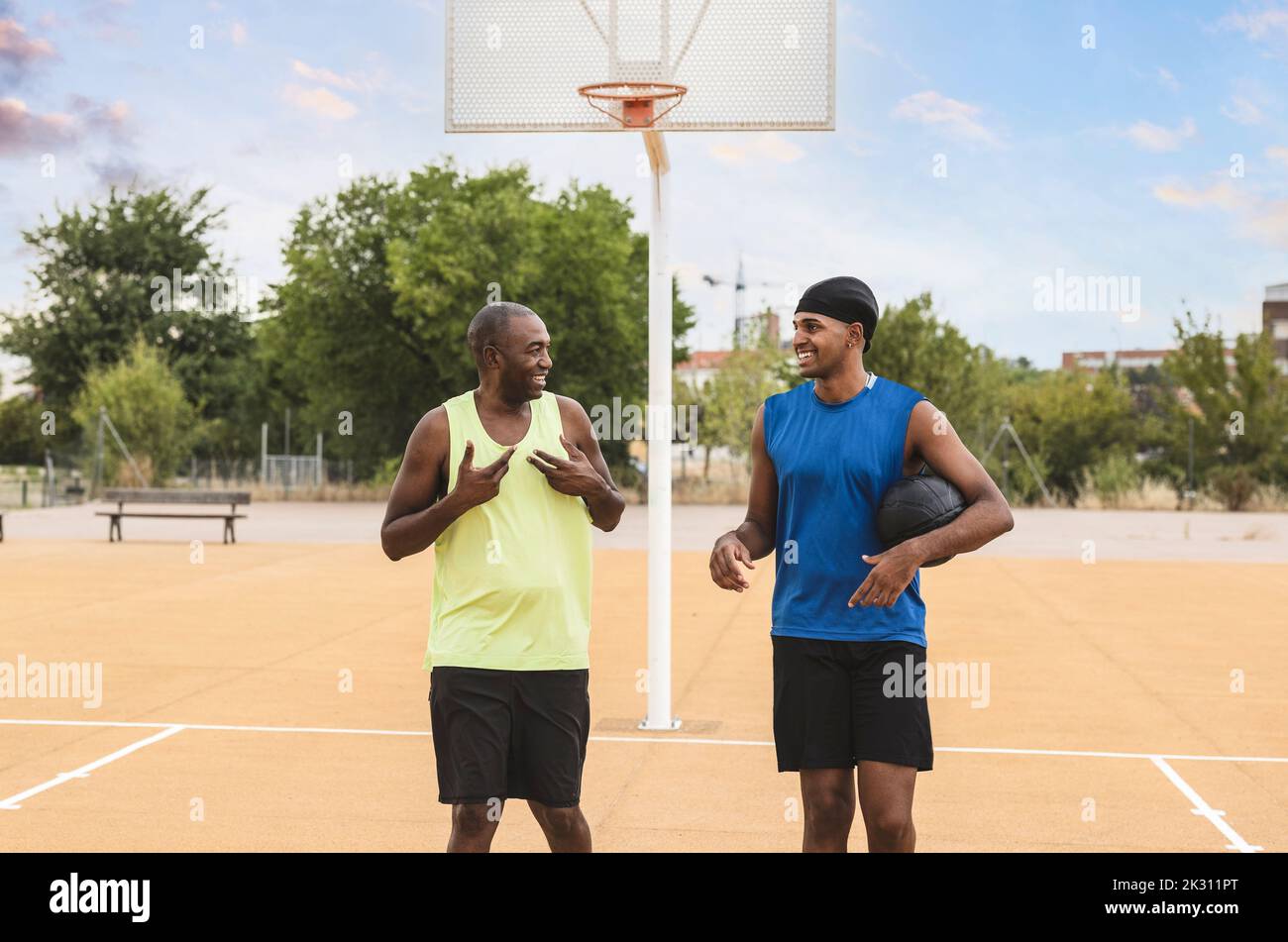 Smiling young man holding ball talking with father at basketball court Stock Photo