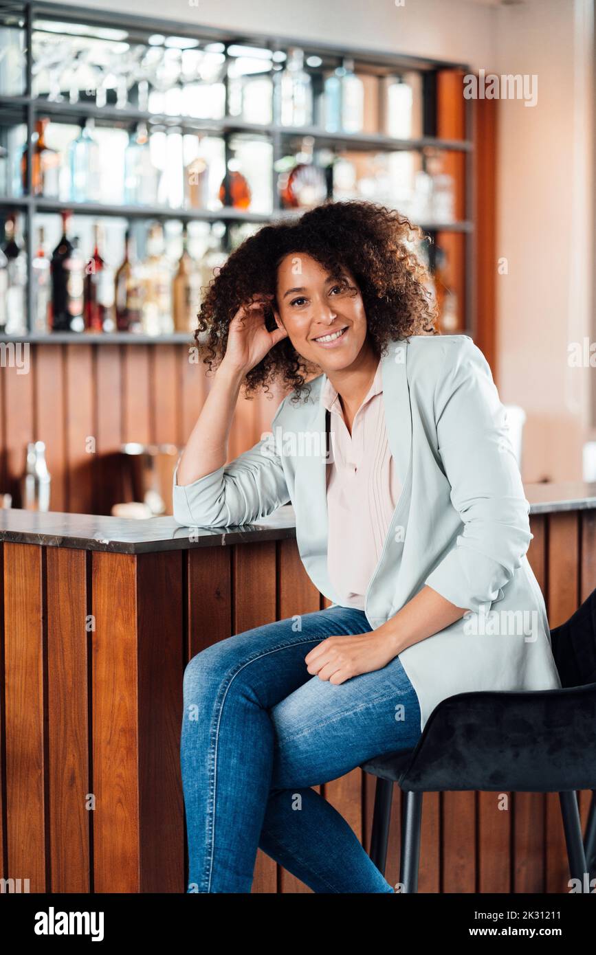 Smiling woman sitting on chair in bar Stock Photo