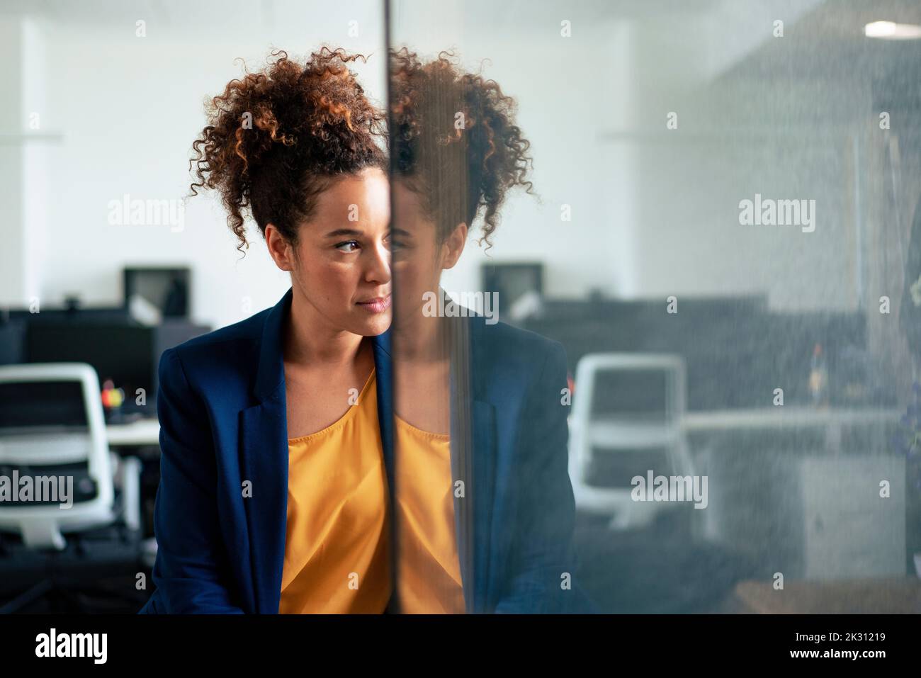 Thoughtful businesswoman with reflection on glass wall in office Stock Photo