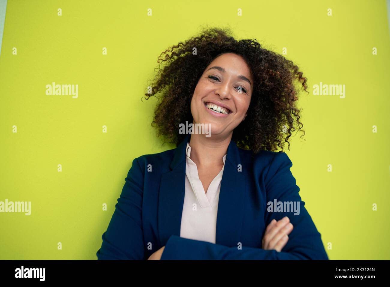 Happy businesswoman with arms crossed in front of wall Stock Photo