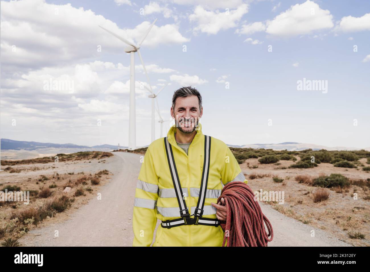 Smiling technician with rope standing at wind farm Stock Photo