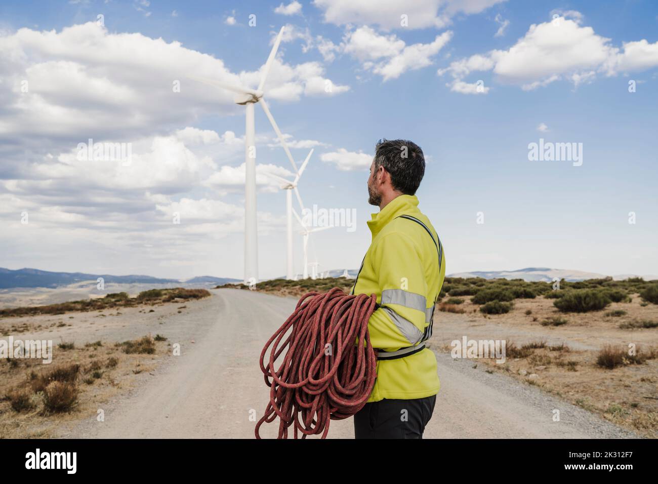 Technician holding rope looking at wind turbines standing on road at wind farm Stock Photo