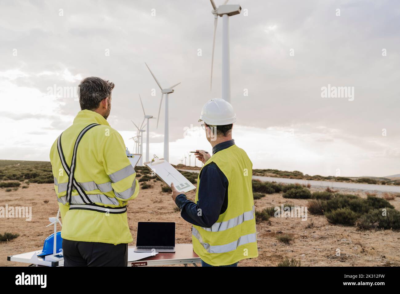 Engineer discussing with colleague looking at wind turbines at wind farm Stock Photo
