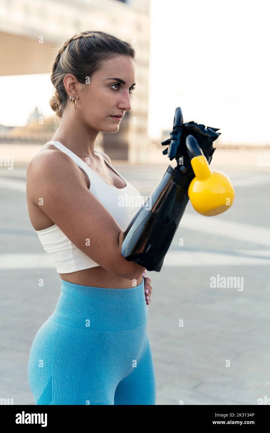 Woman with arm prosthesis exercising using kettlebell Stock Photo