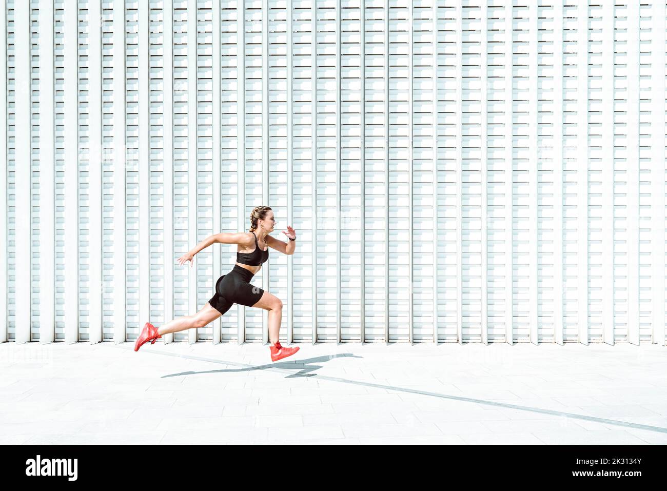 Young athlete running by white wall on sunny day Stock Photo